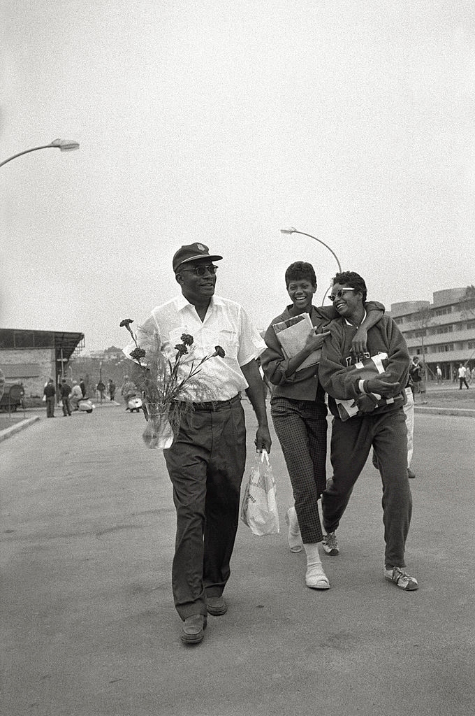 Die US-amerikanische Athletin Wilma Rudolph umarmt eine Kollegin und lächelt. Daneben Trainer Ed Temple mit Blumen in der Hand. Die US-amerikanische Athletin Wilma Rudolph umarmt eine Kollegin und lächelt. Daneben Trainer Ed Temple mit Blumen in der Hand.